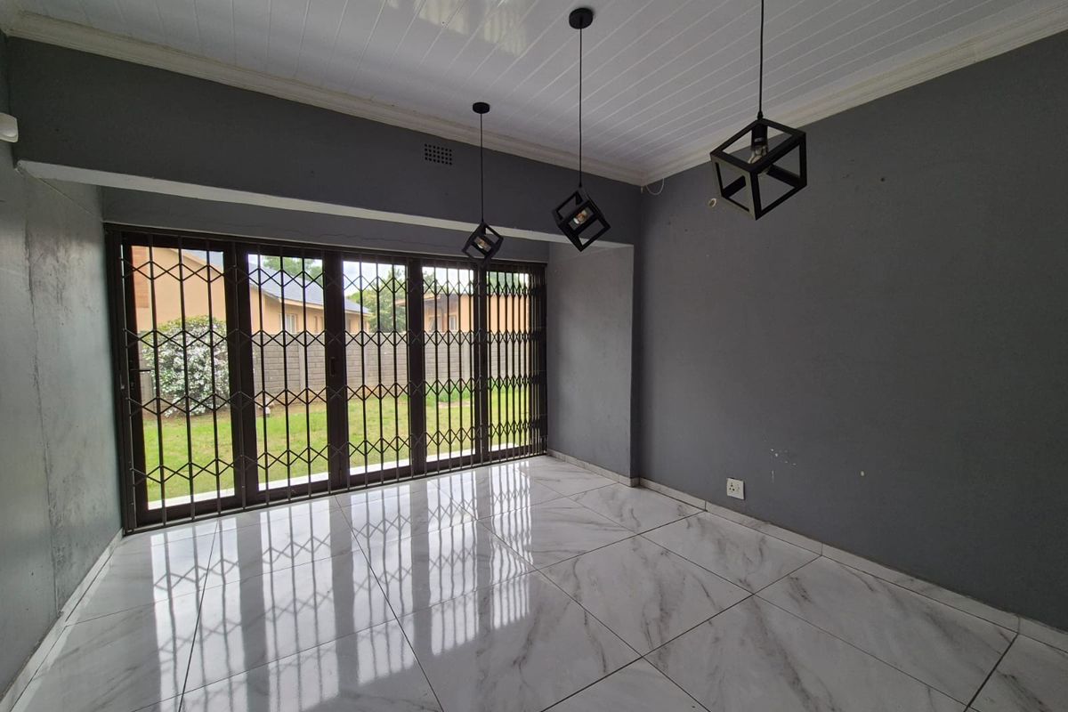 An empty living room featuring modern marble-look floor tiles, pendant lighting, and large sliding glass doors with integrated security gates leading to the garden.