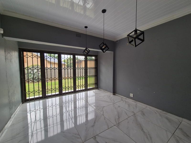 An empty living room featuring modern marble-look floor tiles, pendant lighting, and large sliding glass doors with integrated security gates leading to the garden.