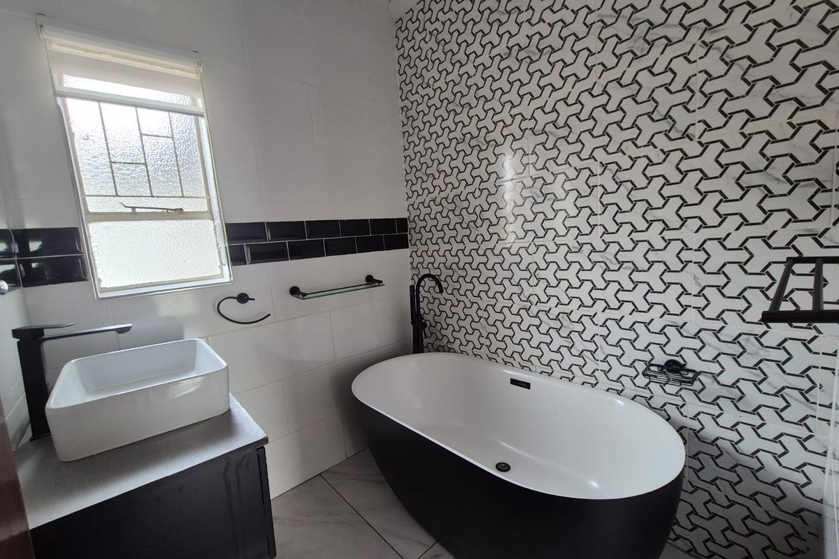 Modern bathroom featuring a sleek freestanding bathtub, vessel sink vanity, and striking geometric patterned feature wall tiles.