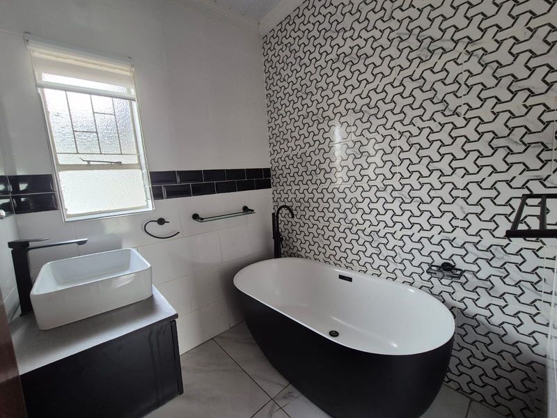 Modern bathroom featuring a sleek freestanding bathtub, vessel sink vanity, and striking geometric patterned feature wall tiles.