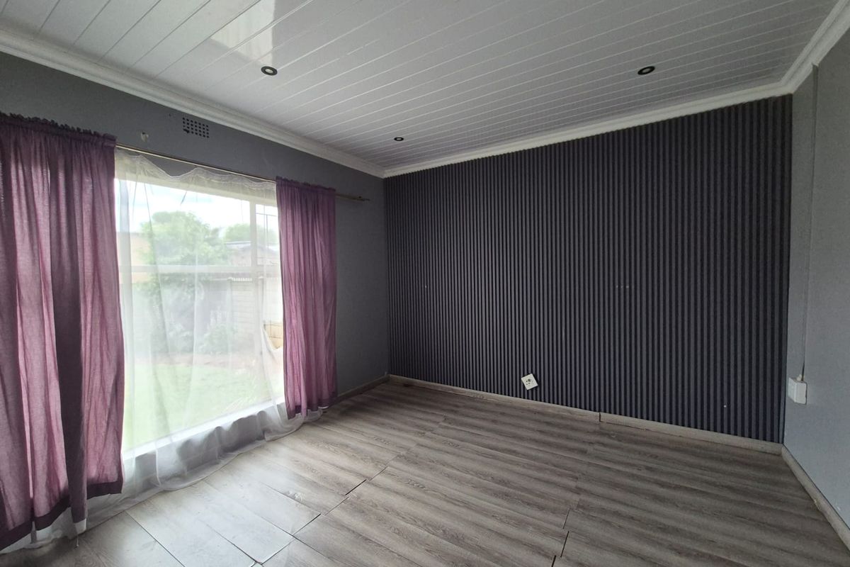An empty bedroom featuring modern slatted wall paneling, laminate flooring, and a clean PVC ceiling with recessed lighting.