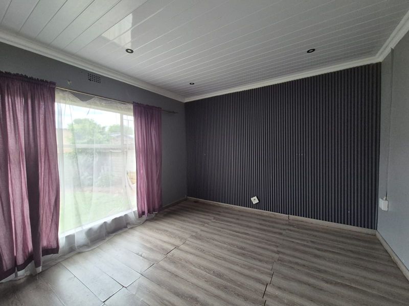 An empty bedroom featuring modern slatted wall paneling, laminate flooring, and a clean PVC ceiling with recessed lighting.