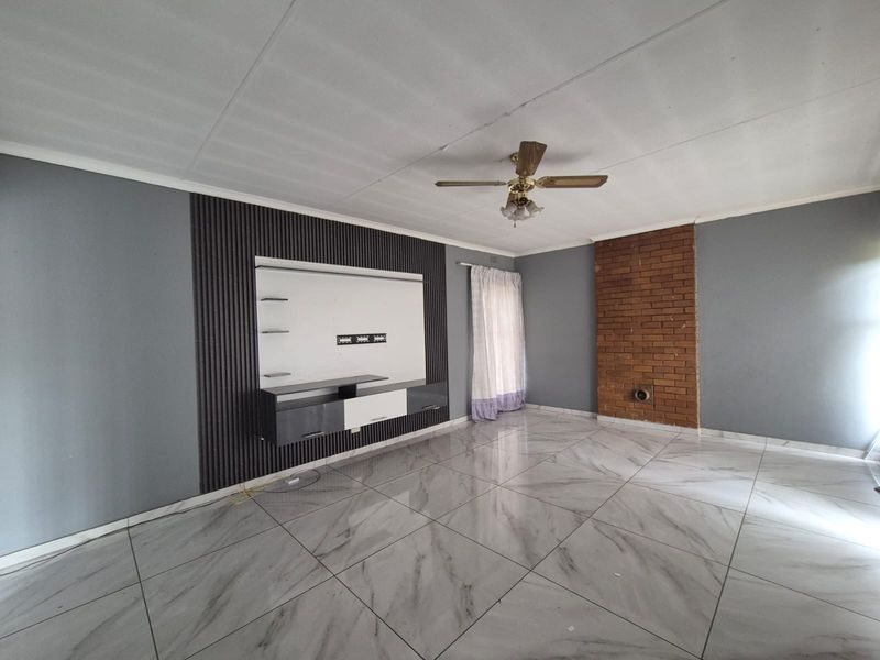 Spacious living room featuring modern marble-look floor tiles, a decorative slatted feature wall with built-in media console, and an exposed brick chimney breast.