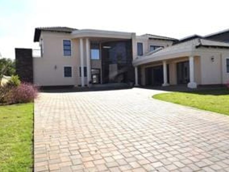 A spacious front exterior view of a modern double-story house featuring a large paved driveway, covered entrance, and well-maintained lawn.