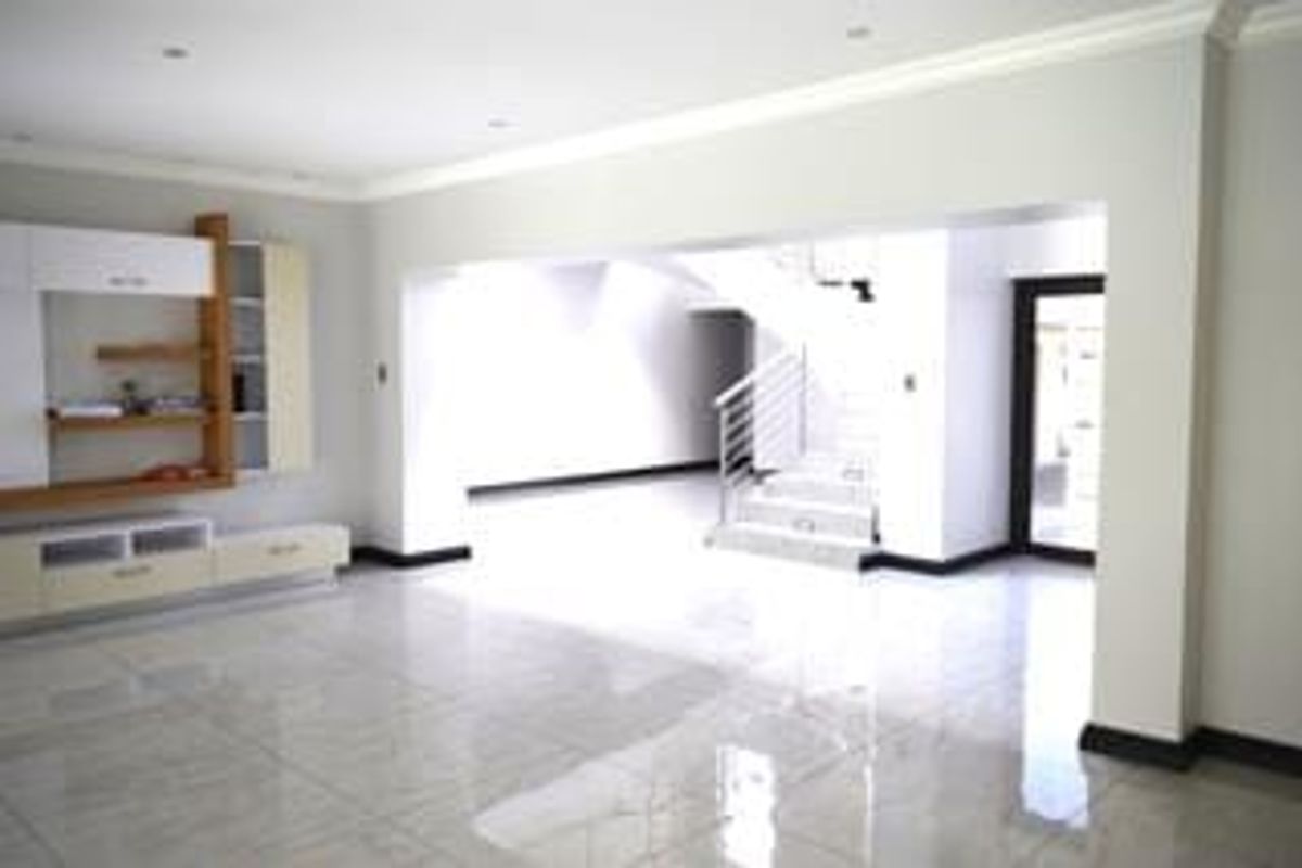 Spacious open-plan living area featuring polished tiled floors, built-in cabinetry, and a modern staircase leading to the upper level.