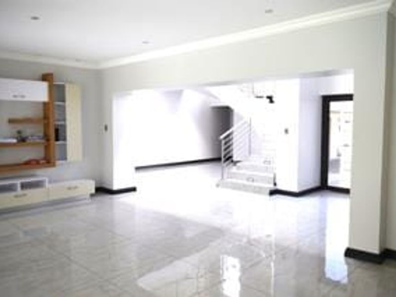 Spacious open-plan living area featuring polished tiled floors, built-in cabinetry, and a modern staircase leading to the upper level.