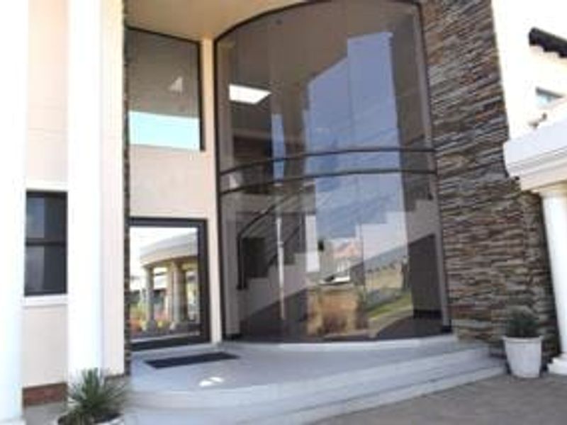 Grand entrance featuring a striking curved glass facade, stone cladding, and elegant columns leading into a spacious foyer with a visible staircase.