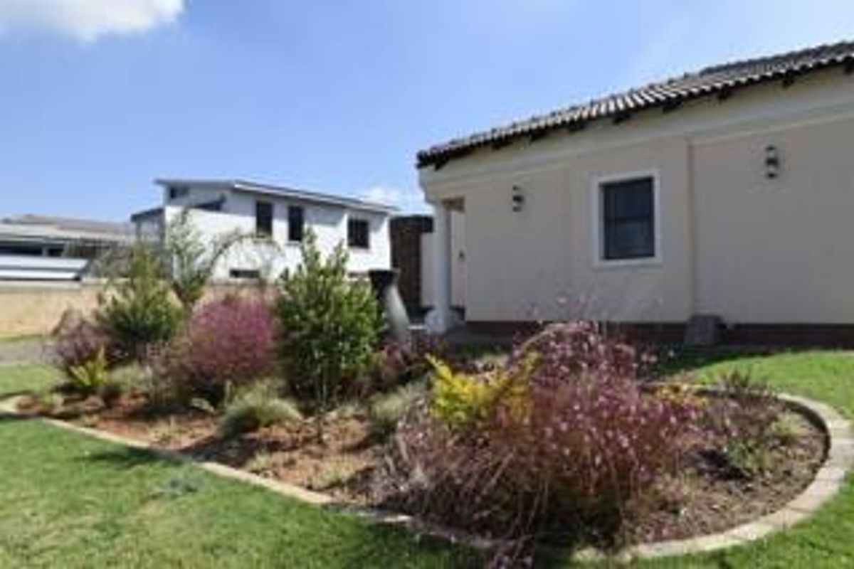 A well-maintained rear exterior view of the property featuring a landscaped garden with brick edging and plastered wall finishes.
