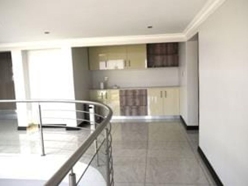 A modern, open-plan kitchenette area featuring high-gloss cabinetry, polished tiled flooring, and a sleek stainless steel balustrade overlooking the lower level.