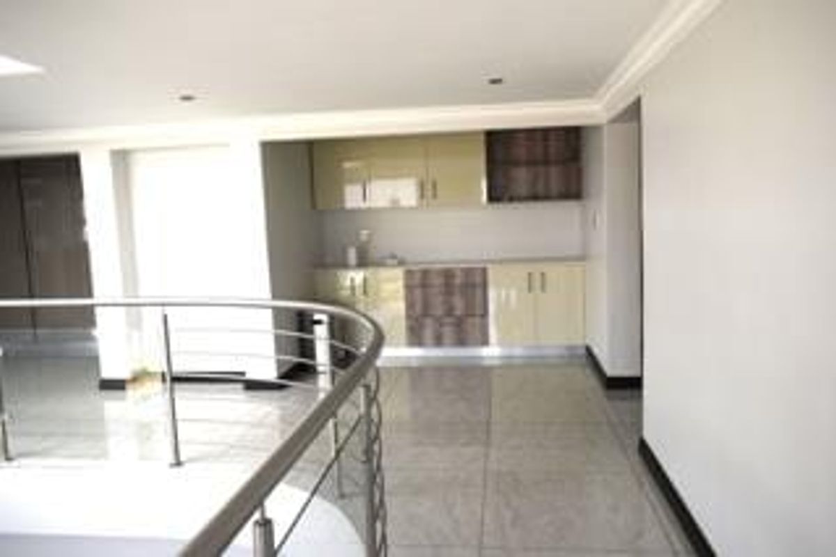A modern, open-plan kitchenette area featuring high-gloss cabinetry, polished tiled flooring, and a sleek stainless steel balustrade overlooking the lower level.