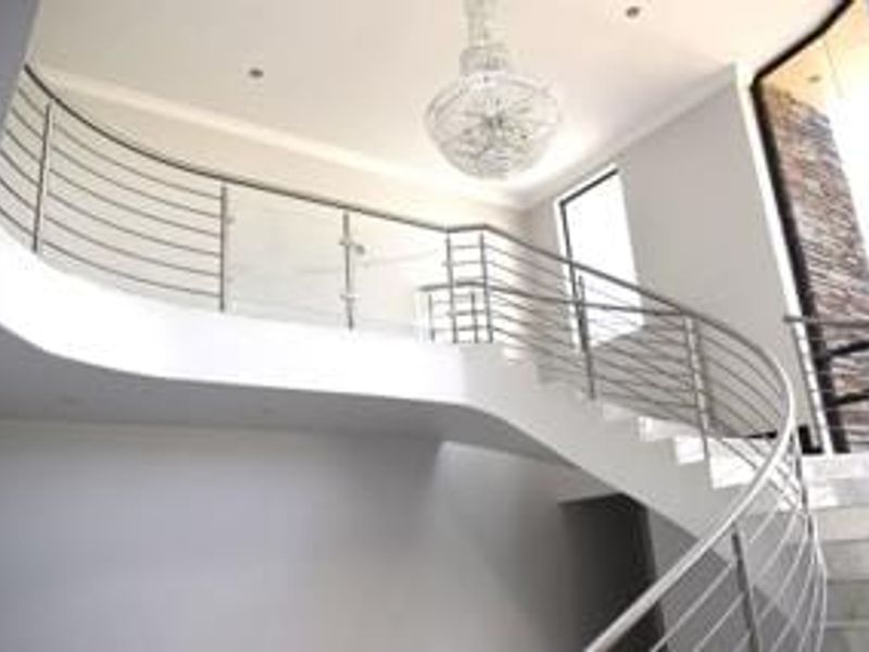 Elegant entrance foyer featuring a striking curved staircase with stainless steel and glass balustrades, complemented by a stone feature wall and modern chandelier.