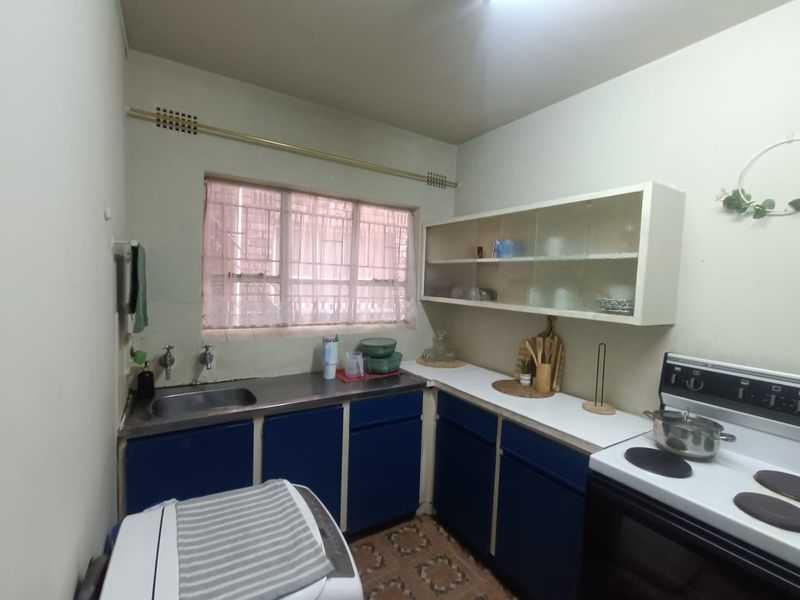 A compact kitchen featuring blue cabinetry, a stainless steel sink, and an electric stove, offering a functional layout with potential for modern updates.