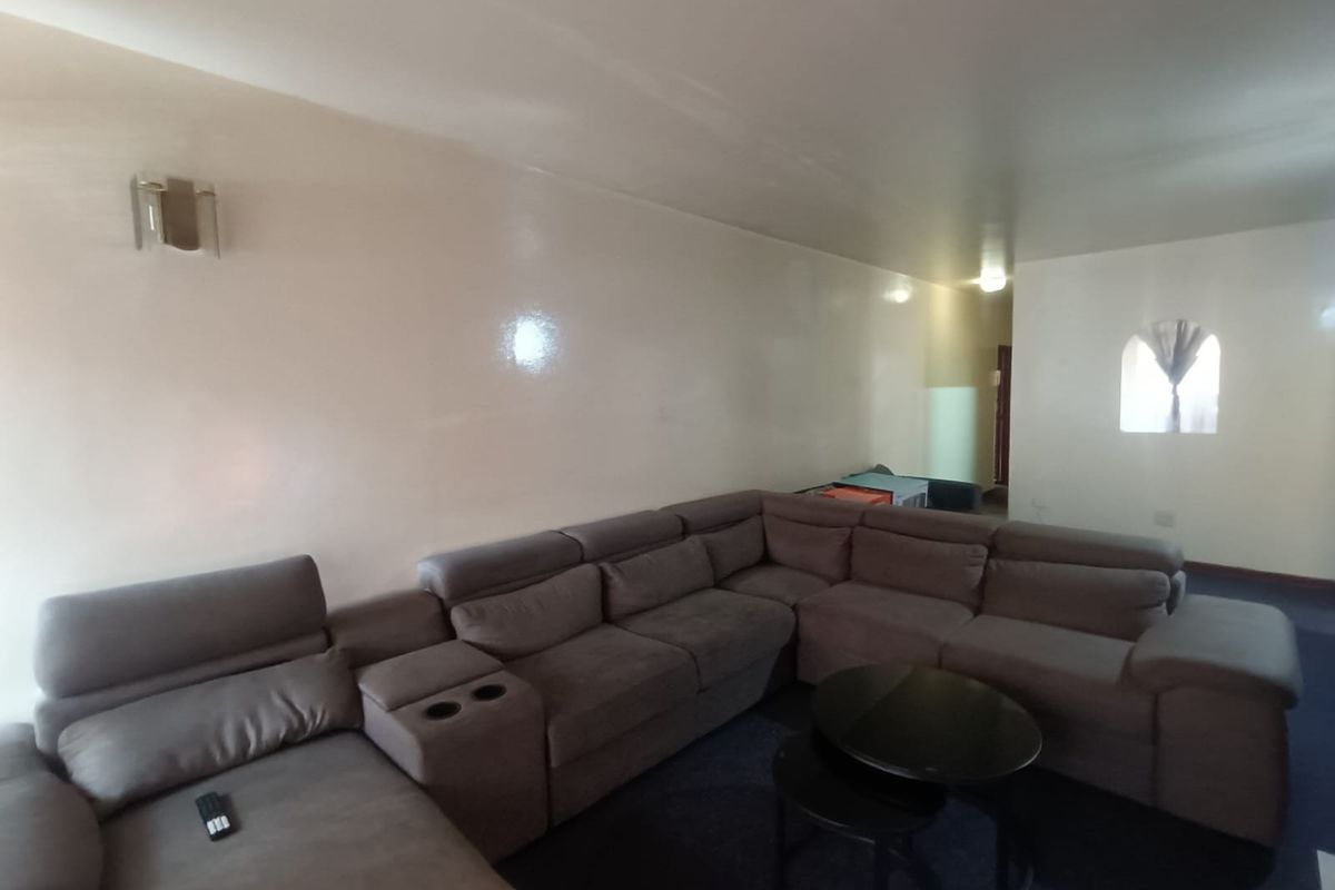 A spacious living room featuring neutral walls, a wall-mounted light fixture, and an arched window, providing a blank canvas for interior design.