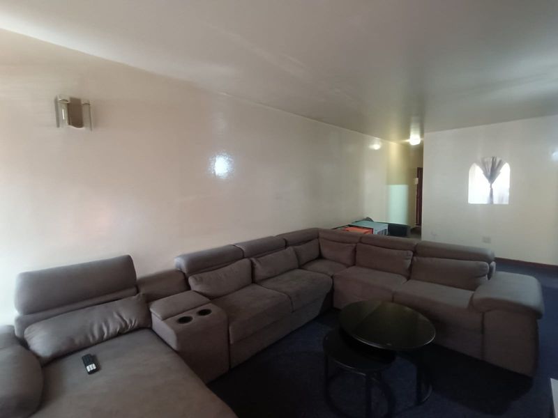 A spacious living room featuring neutral walls, a wall-mounted light fixture, and an arched window, providing a blank canvas for interior design.