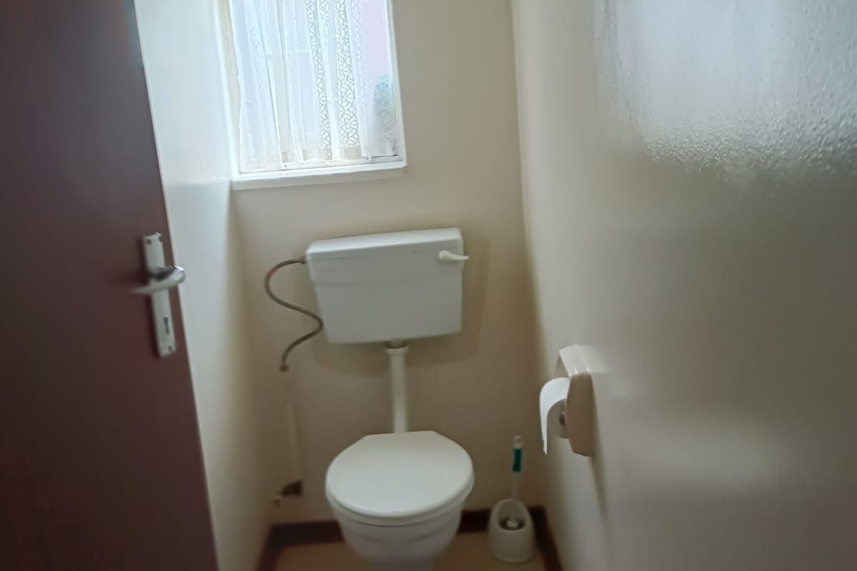 A compact, functional bathroom featuring a standard toilet, tiled flooring, and a window providing natural light.