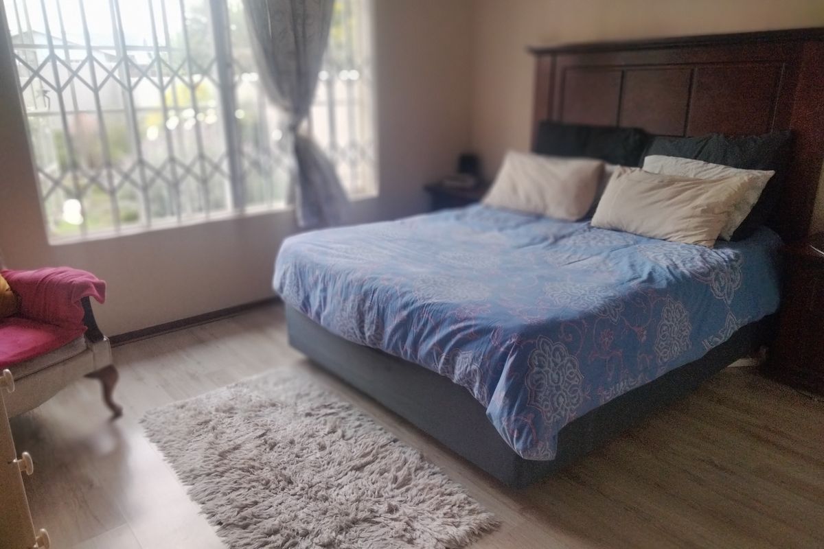 A bedroom featuring light-toned laminate flooring and a large window fitted with a security gate for added protection.
