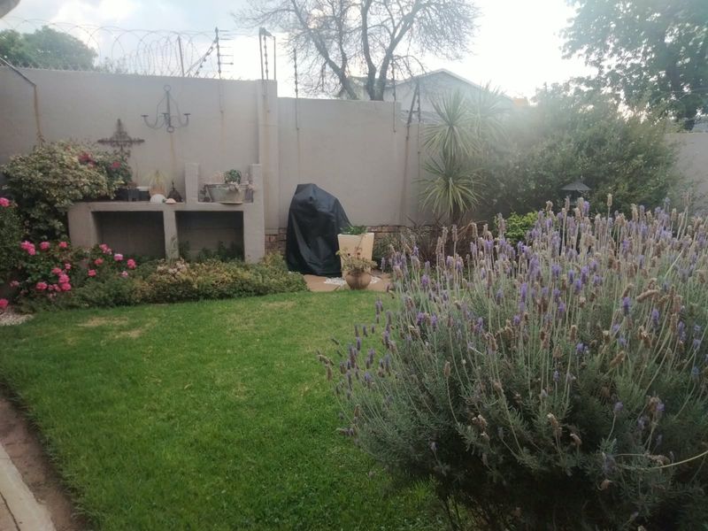 A well-maintained private garden featuring a built-in braai area, lush lawn, established lavender plants, and secure perimeter walling with electric fencing.