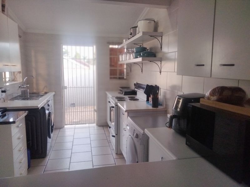 Functional kitchen featuring white cabinetry, tiled backsplash, open shelving, and direct access to an exterior security gate.