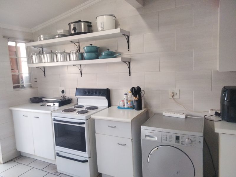 A functional kitchen featuring white cabinetry, tiled backsplash, open shelving, and a freestanding stove with integrated laundry appliance space.