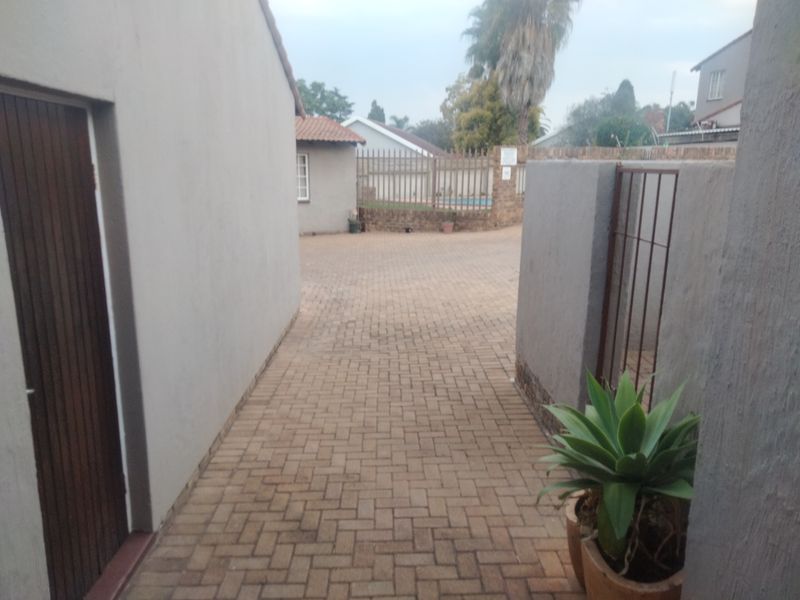 A paved rear courtyard area featuring a boundary wall, metal security gate, and access to the main building structure.