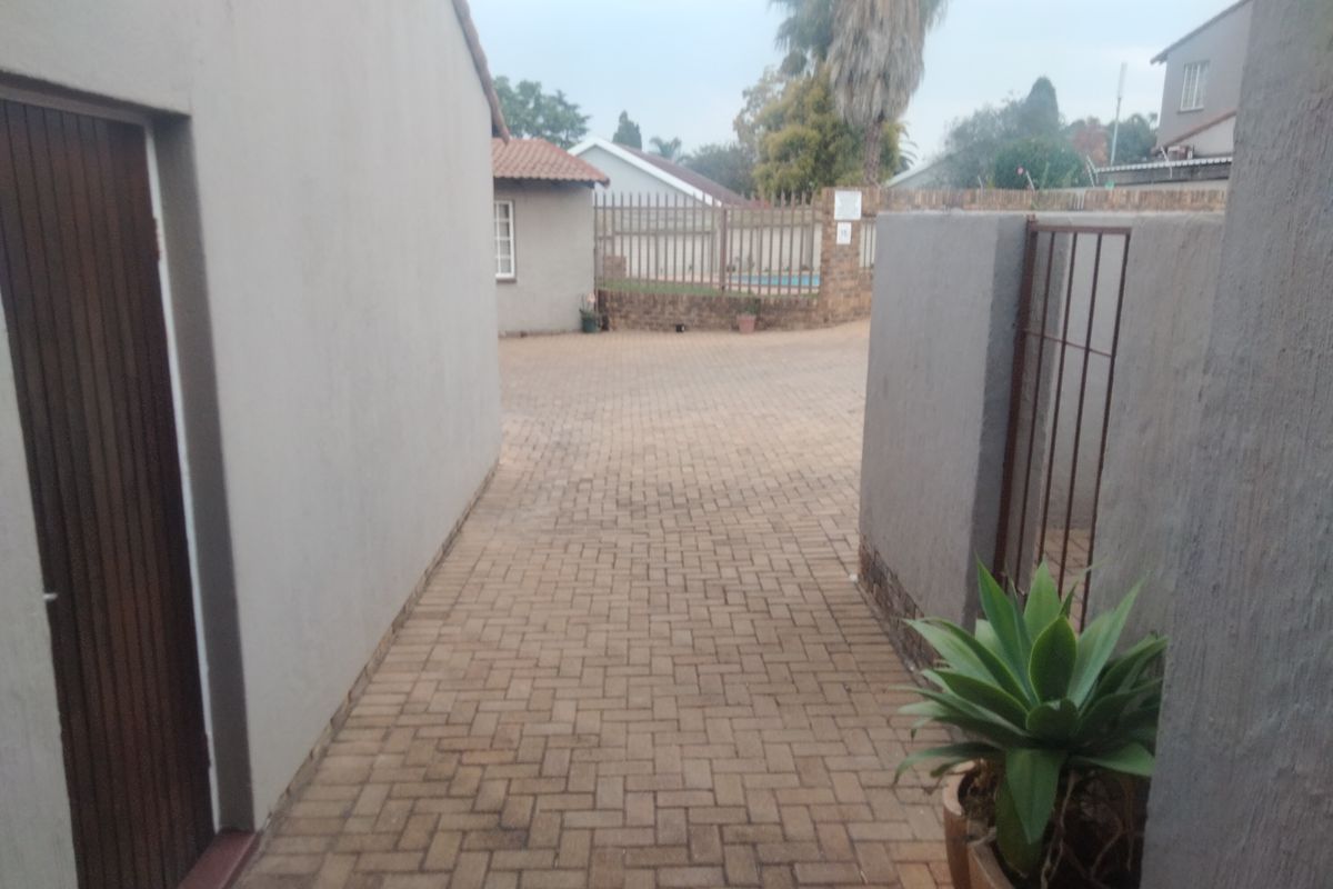 A paved rear courtyard area featuring a boundary wall, metal security gate, and access to the main building structure.