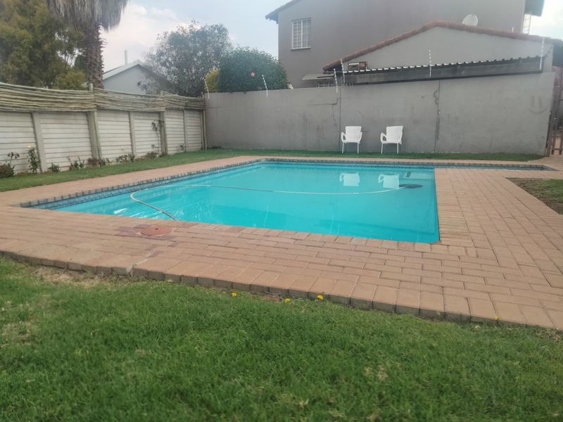 A private outdoor swimming pool area featuring brick paving, a surrounding lawn, and a secure boundary wall with electric fencing.