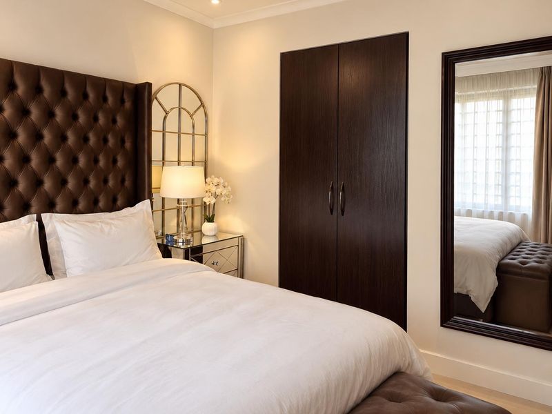 A well-appointed bedroom featuring a dark wood built-in wardrobe, recessed ceiling lighting, and elegant coving details.