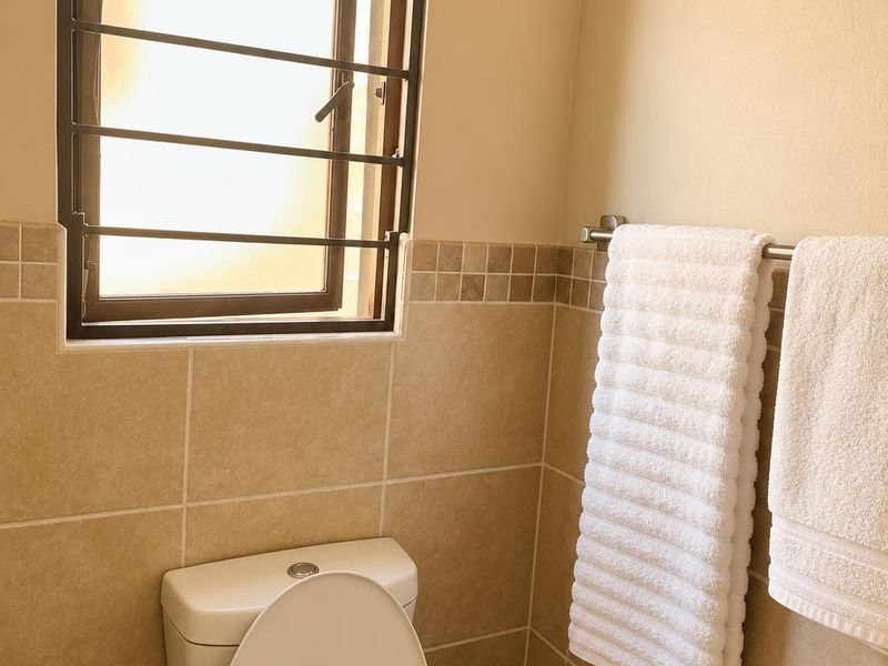 A functional bathroom featuring neutral wall tiling, a standard toilet, and a window fitted with security bars.