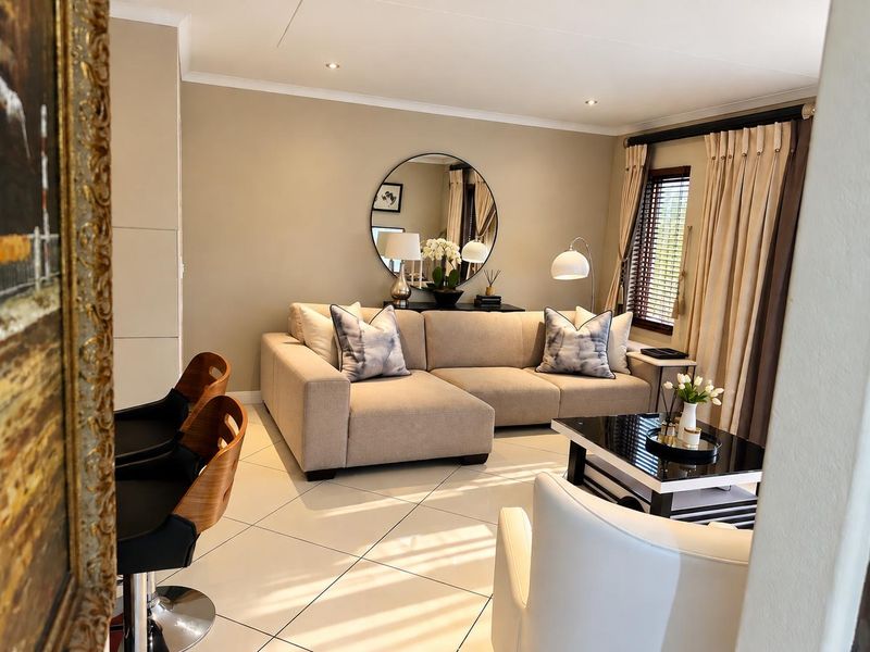 A well-maintained living room featuring neutral wall tones, tiled flooring, and natural light filtered through venetian blinds and curtains.