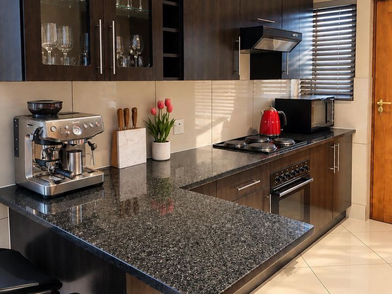 Modern kitchen featuring dark wood cabinetry, granite countertops, built-in oven, electric hob, extractor fan, and tiled flooring with a breakfast bar area.