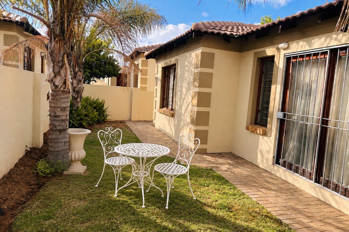 A well-maintained rear garden area featuring a paved walkway, lawn, and direct access to the townhouse interior via a sliding door with security gate.