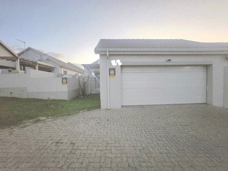 Front exterior view of the townhouse featuring a paved driveway, single garage door, and secure boundary wall.