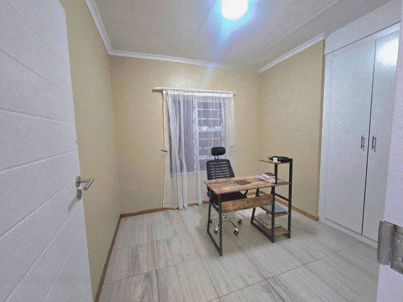 A functional bedroom featuring tiled flooring, a built-in wardrobe, and a window fitted with a security gate.