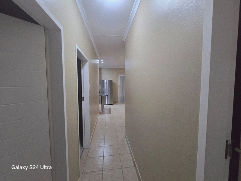A neutral-toned hallway with tiled flooring leading towards an open-plan living area, featuring clean lines and simple architectural finishes.