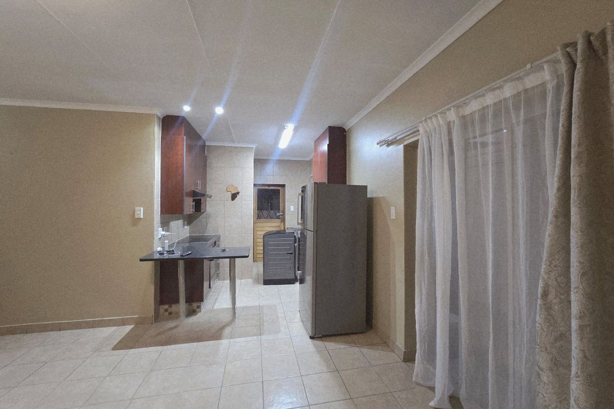 A functional kitchen featuring tiled flooring, built-in cabinetry, a breakfast bar, and a tiled backsplash, leading to an adjacent utility area.