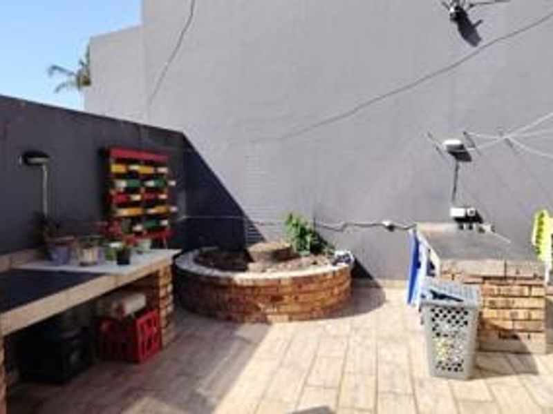 Outdoor patio area featuring a built-in brick braai, tiled flooring, and a central circular brick planter, offering a functional space for outdoor entertainment.