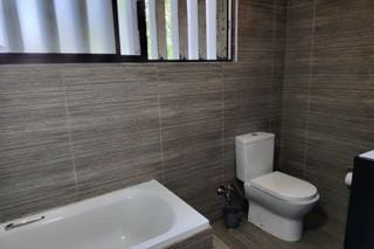 A clean bathroom featuring full-height textured wall tiling, a standard bathtub, and a modern toilet with a louver window for ventilation.