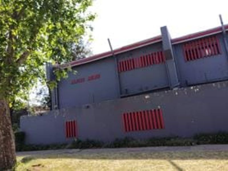Exterior view of the townhouse facade featuring a boundary wall and security louvers, showing signs of weathered paintwork.