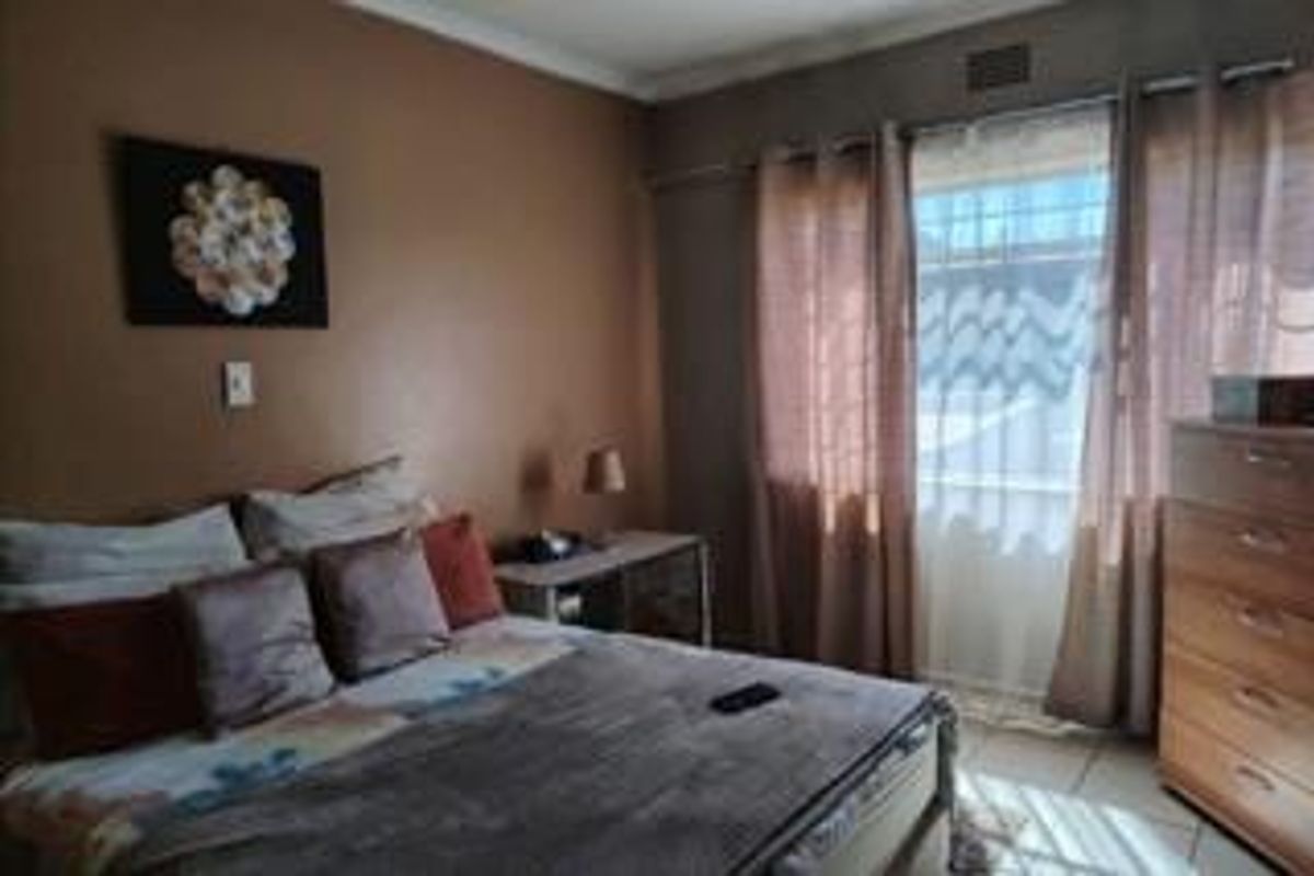 A standard bedroom featuring tiled flooring, a window with security bars, and coving detail, offering a functional space ready for personal updates.