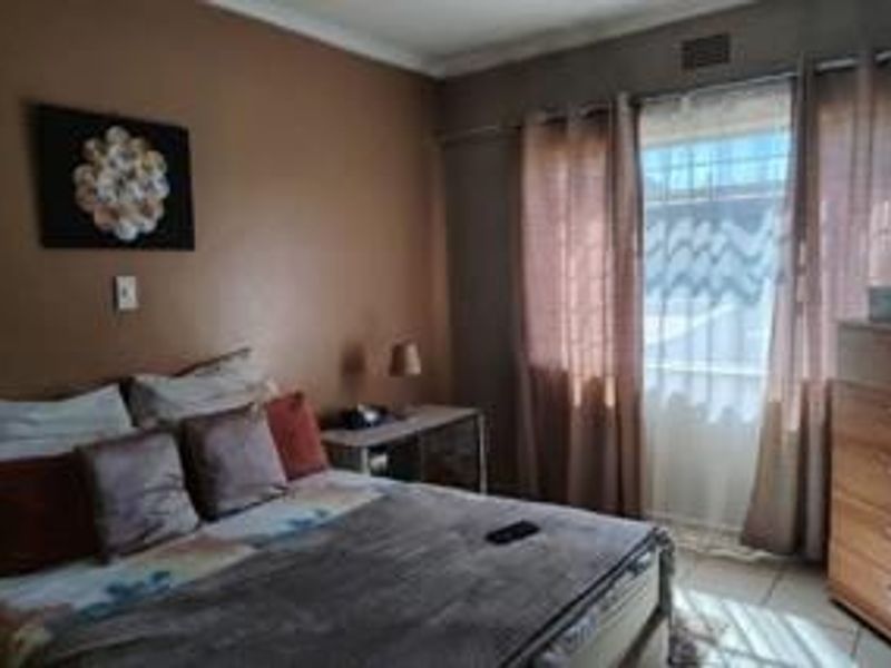 A standard bedroom featuring tiled flooring, a window with security bars, and coving detail, offering a functional space ready for personal updates.