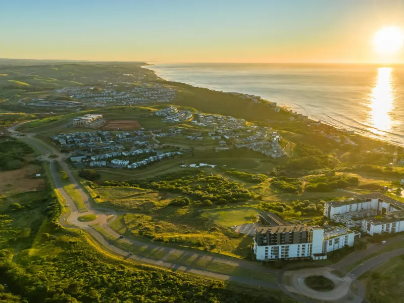 An expansive aerial view of a coastal residential estate at sunset, showcasing the surrounding landscape and proximity to the ocean.