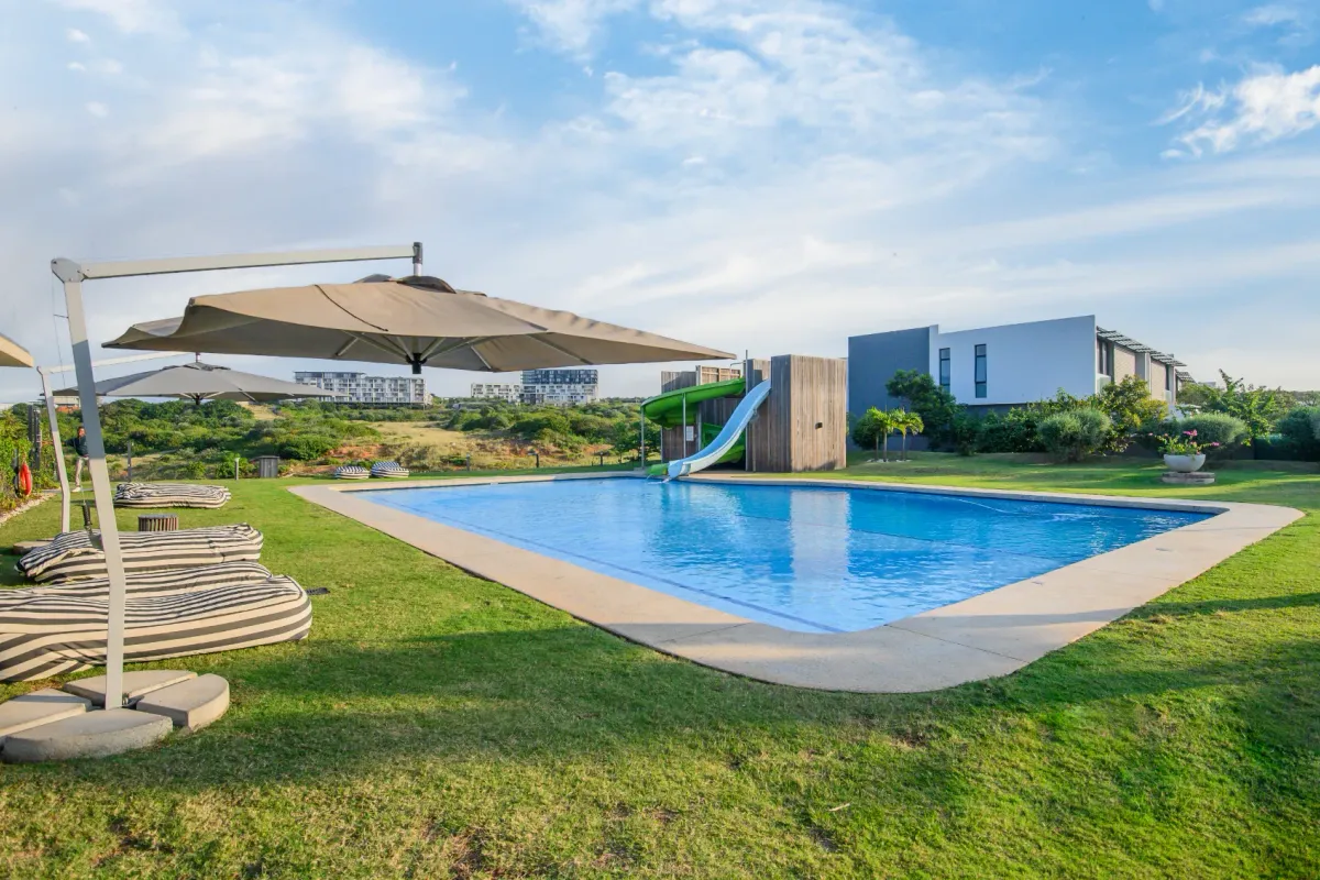 A well-maintained outdoor swimming pool area featuring a built-in slide, surrounded by landscaped lawn and open views.