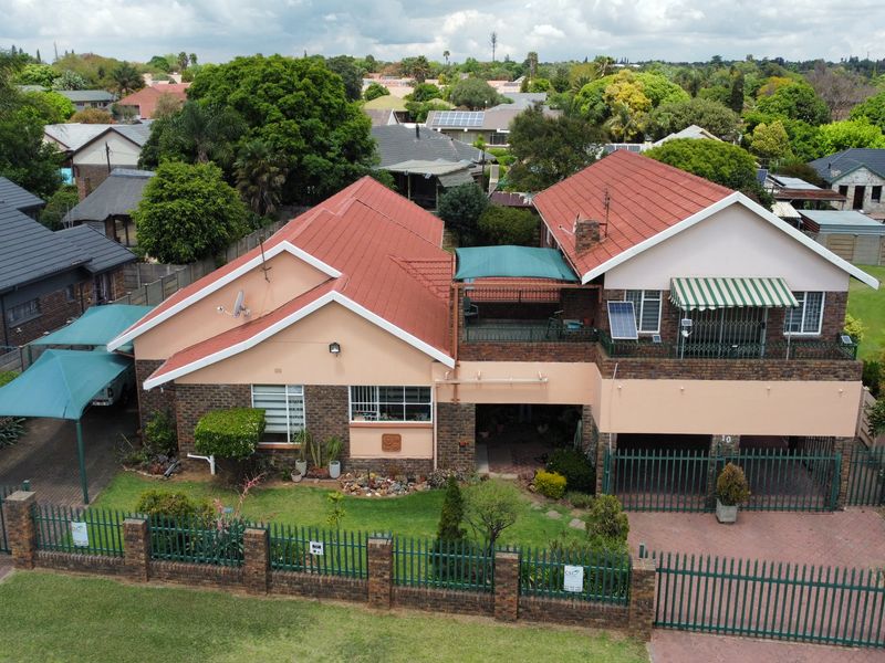 Aerial view of a residential property featuring a multi-level tiled roof, brick exterior, paved driveway, perimeter fencing, and an attached balcony.