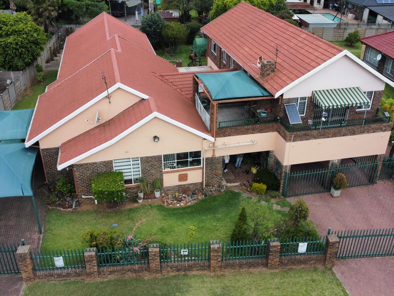 Aerial view of a multi-level residential property featuring a tiled roof, paved driveway, balcony, and established garden with perimeter fencing.