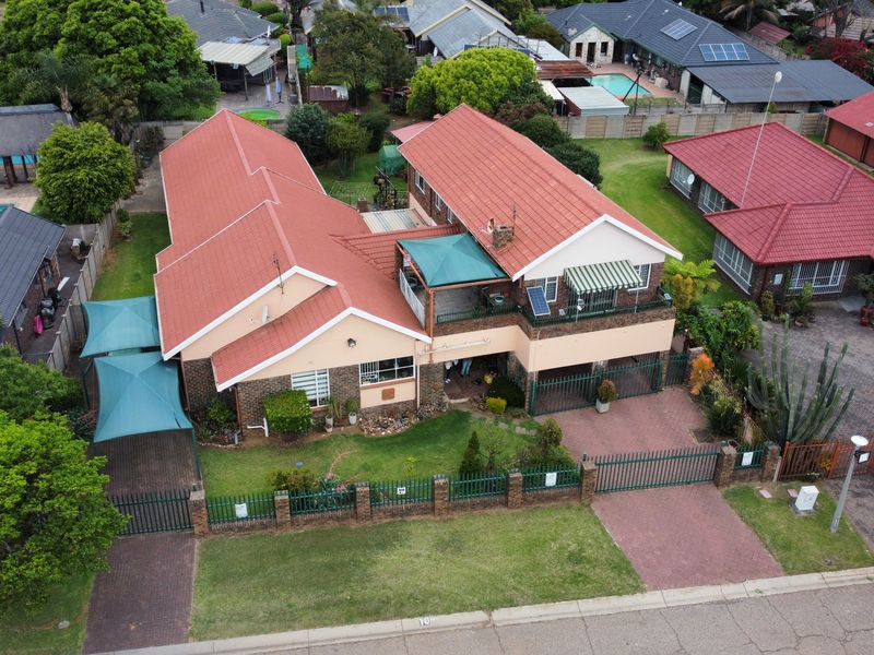 Aerial view of a residential property featuring a tiled roof, paved driveway, perimeter fencing, and an attached balcony.