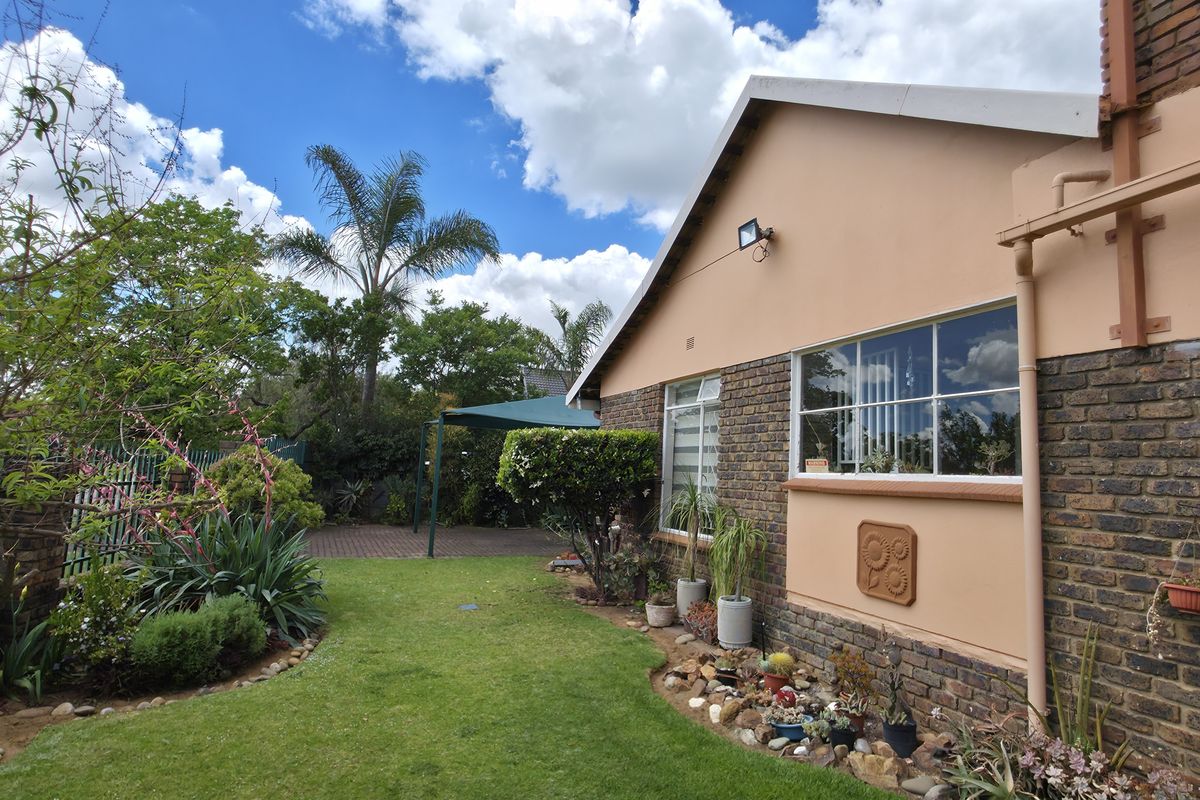 A well-maintained rear exterior view featuring a brick facade, steel-framed windows, and a landscaped garden with a paved patio area.