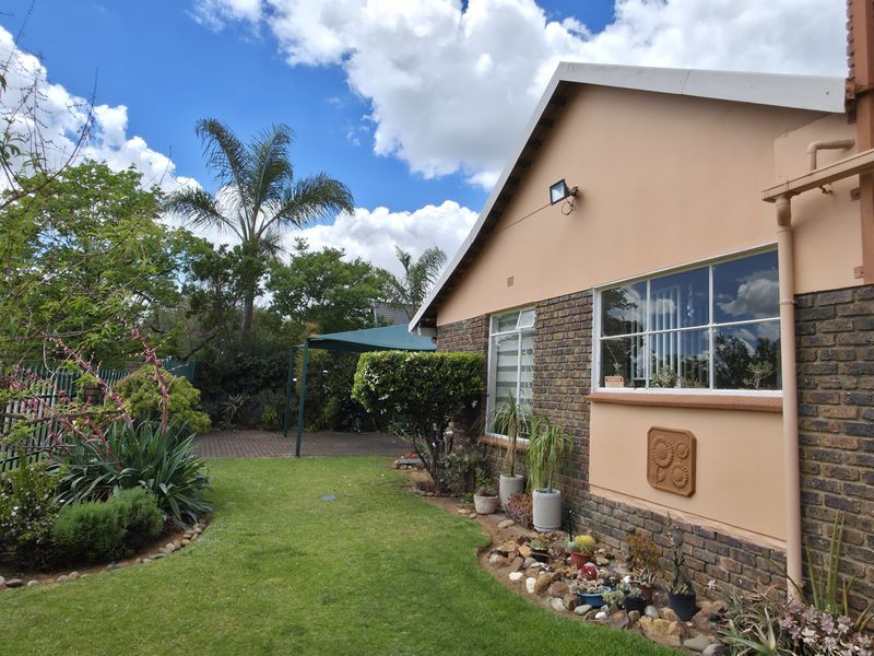 A well-maintained rear exterior view featuring a brick facade, steel-framed windows, and a landscaped garden with a paved patio area.