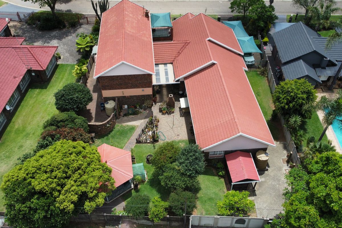 Aerial view of a residential property featuring a tiled roof, landscaped garden, swimming pool, and paved outdoor areas.
