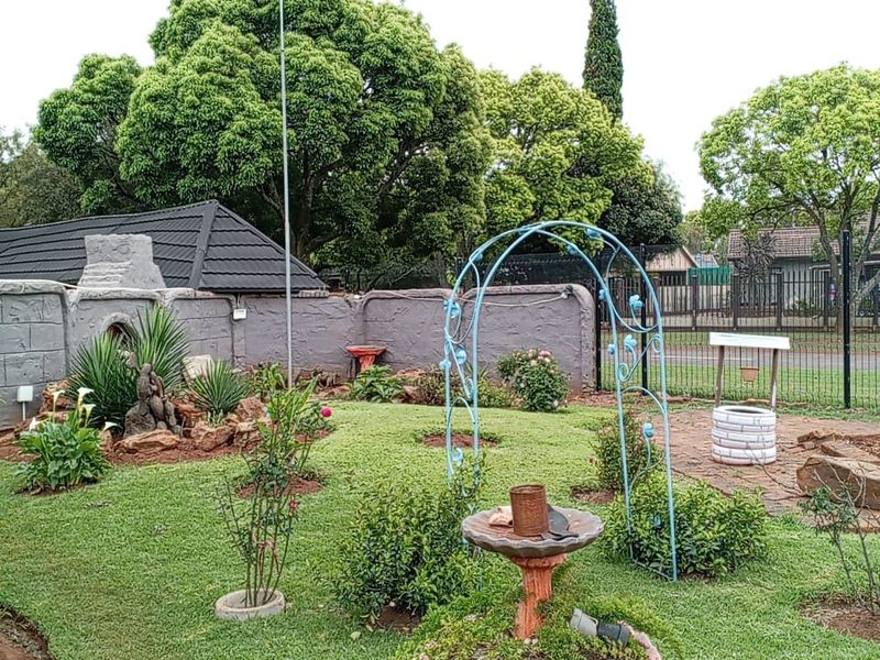 A landscaped garden featuring a brick boundary wall, a built-in outdoor fireplace, and a paved section enclosed by perimeter fencing.