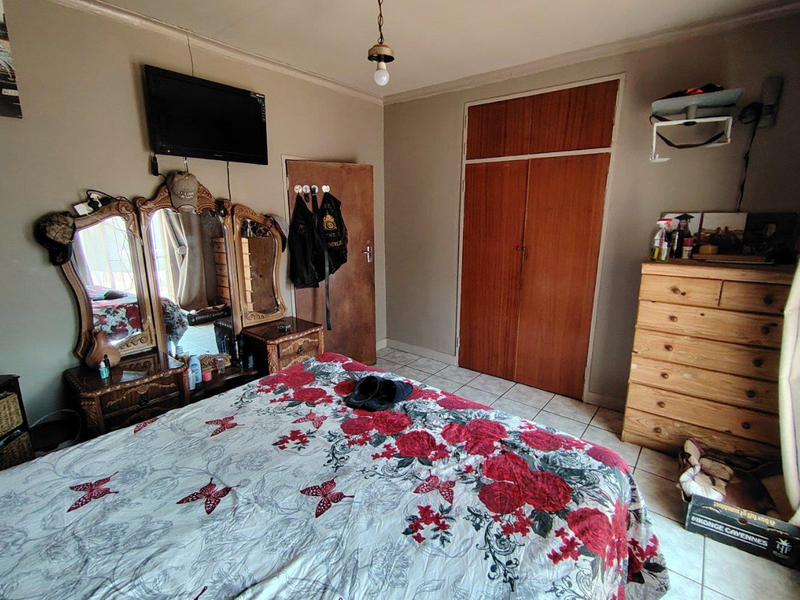 A functional bedroom featuring tiled flooring and a built-in wooden wardrobe, providing essential storage space within the room.